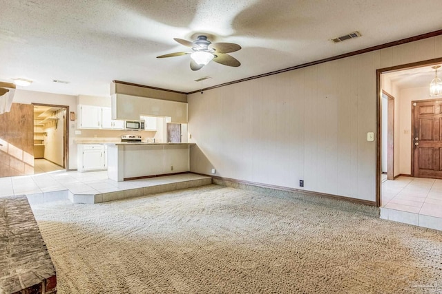 unfurnished living room featuring ceiling fan, light colored carpet, a textured ceiling, and wooden walls