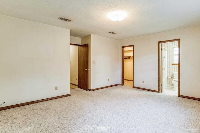 unfurnished bedroom featuring a walk in closet, ensuite bathroom, a closet, and light carpet