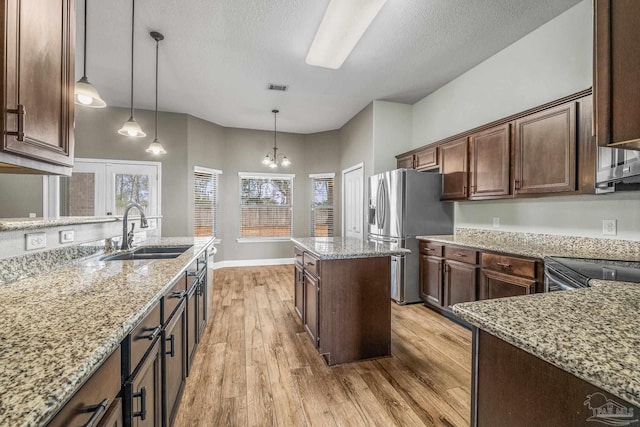 kitchen with light stone counters, appliances with stainless steel finishes, decorative light fixtures, and sink