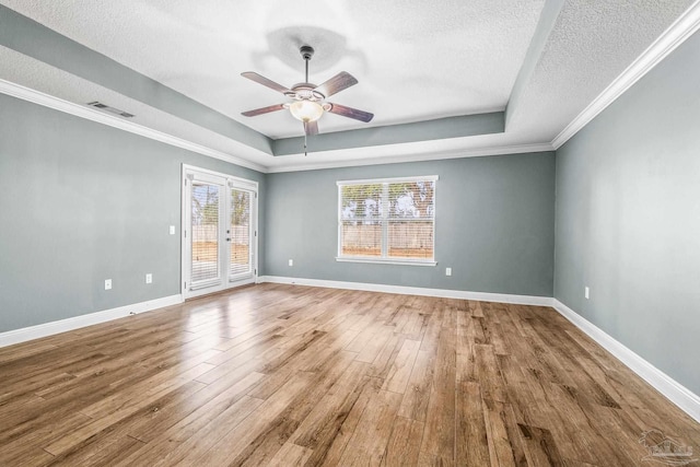 empty room with crown molding, ceiling fan, hardwood / wood-style floors, a tray ceiling, and a textured ceiling