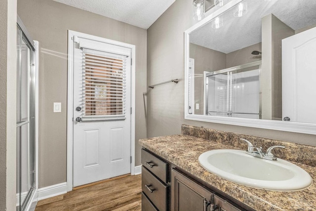 bathroom with hardwood / wood-style flooring, vanity, a shower with door, and a textured ceiling