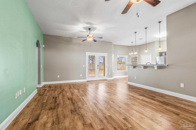 unfurnished living room with ceiling fan with notable chandelier, light hardwood / wood-style floors, and a textured ceiling