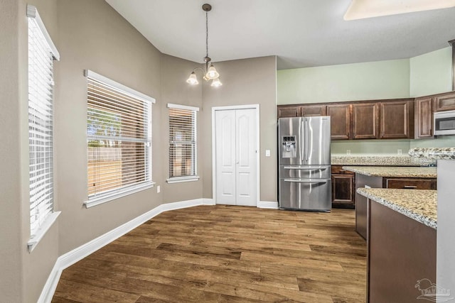 kitchen with hanging light fixtures, hardwood / wood-style flooring, stainless steel appliances, light stone countertops, and dark brown cabinets