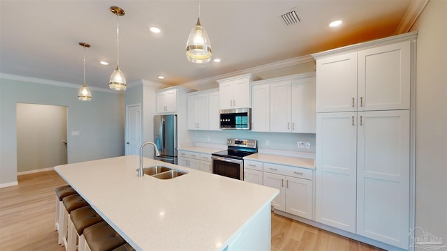 kitchen featuring an island with sink, sink, stainless steel appliances, and decorative light fixtures