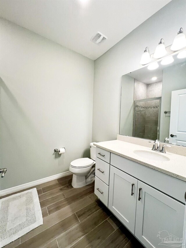 bathroom featuring hardwood / wood-style flooring, a shower with door, vanity, and toilet