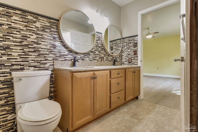 bathroom featuring toilet, a sink, tile walls, decorative backsplash, and double vanity