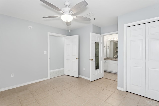 unfurnished bedroom featuring ensuite bathroom, sink, light tile patterned floors, a closet, and ceiling fan