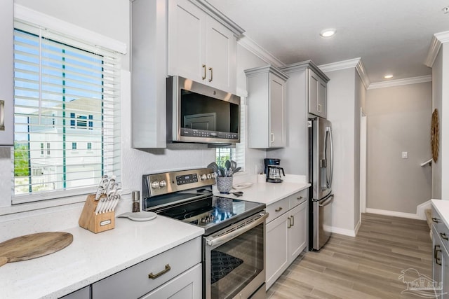 kitchen with gray cabinetry, crown molding, light hardwood / wood-style flooring, and stainless steel appliances