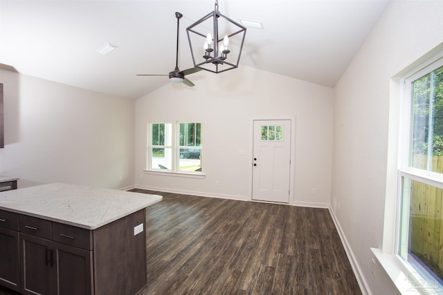 interior space with ceiling fan with notable chandelier, dark brown cabinetry, vaulted ceiling, dark wood-type flooring, and pendant lighting