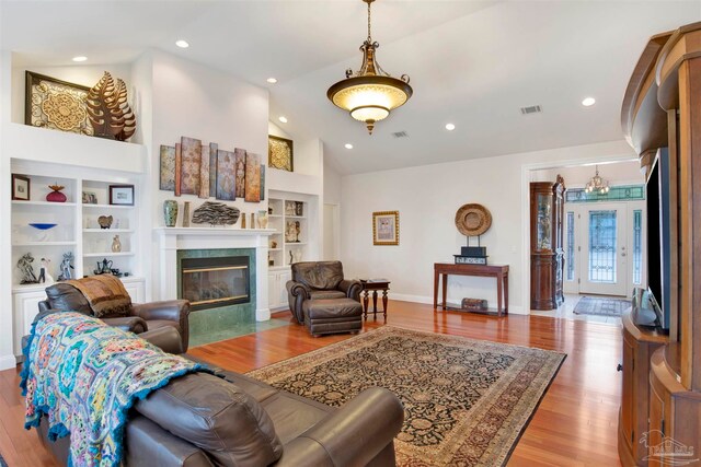 living room with a tile fireplace, high vaulted ceiling, built in features, and light wood-type flooring