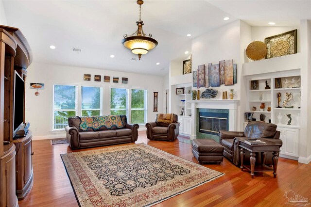 living room with high vaulted ceiling, a tiled fireplace, hardwood / wood-style floors, and built in features