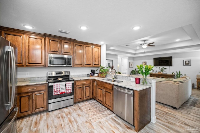 kitchen featuring a raised ceiling, sink, kitchen peninsula, stainless steel appliances, and light hardwood / wood-style flooring