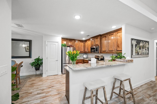 kitchen with light stone counters, a kitchen breakfast bar, kitchen peninsula, stainless steel appliances, and light hardwood / wood-style floors