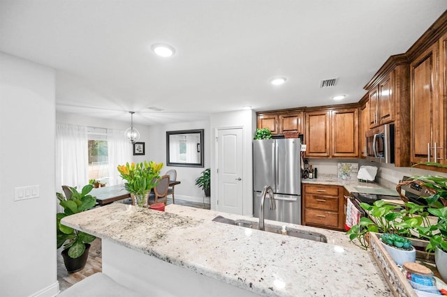 kitchen with sink, hanging light fixtures, kitchen peninsula, stainless steel appliances, and light stone countertops