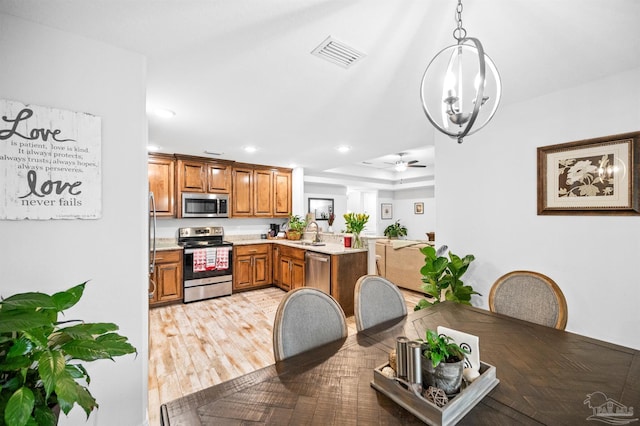 dining room featuring ceiling fan with notable chandelier, a tray ceiling, light hardwood / wood-style floors, and sink