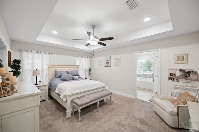 carpeted bedroom featuring a raised ceiling, ensuite bathroom, and ceiling fan