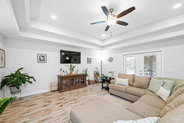 living room featuring a raised ceiling, light hardwood / wood-style flooring, ceiling fan, and french doors