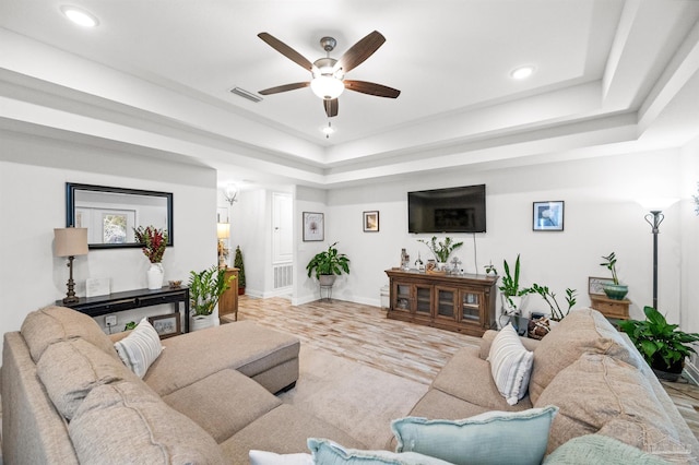 living room with a raised ceiling, ceiling fan, and light hardwood / wood-style floors