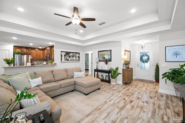 living room featuring a tray ceiling, light hardwood / wood-style floors, and ceiling fan