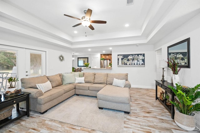 living room featuring french doors, ceiling fan, light wood-type flooring, and a tray ceiling