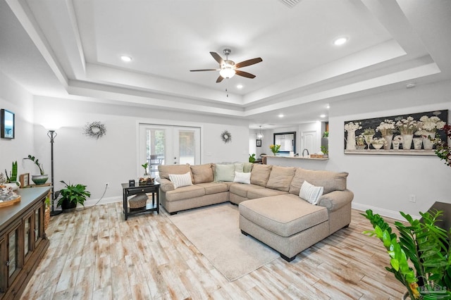 living room with a raised ceiling, ceiling fan, light wood-type flooring, and french doors