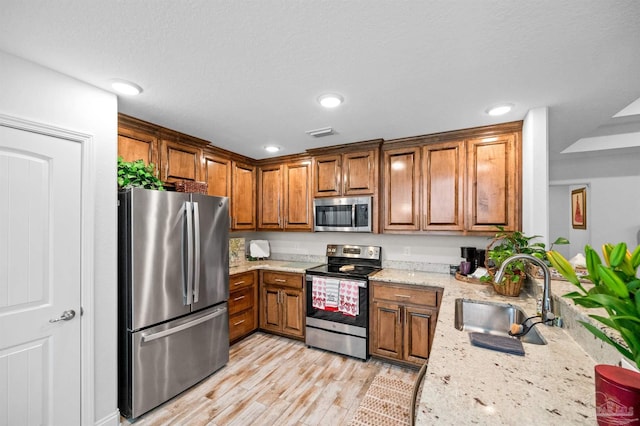 kitchen featuring sink, light hardwood / wood-style floors, stainless steel appliances, light stone countertops, and a textured ceiling