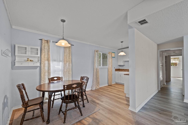 dining area featuring visible vents, baseboards, crown molding, and light wood finished floors