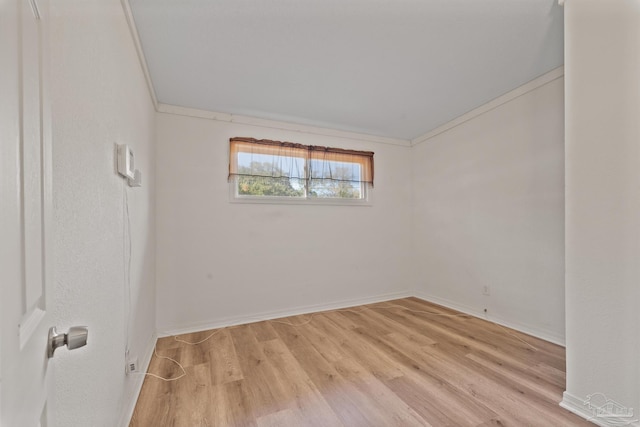 empty room with crown molding, light wood-type flooring, and baseboards