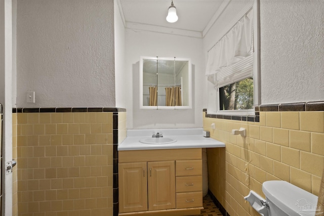 full bathroom with a wainscoted wall, toilet, vanity, a textured wall, and tile walls