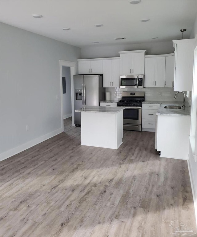 kitchen featuring a kitchen island, light countertops, white cabinets, a sink, and appliances with stainless steel finishes