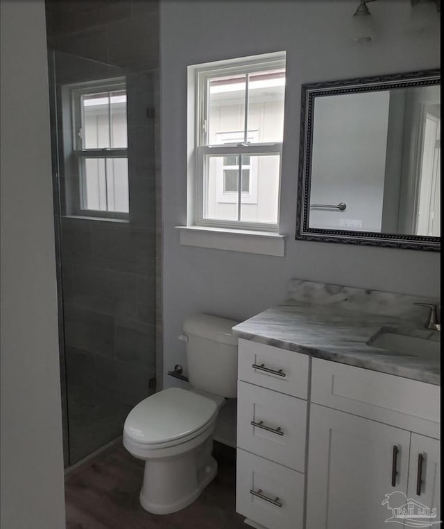 full bathroom with vanity, toilet, tiled shower, and wood finished floors