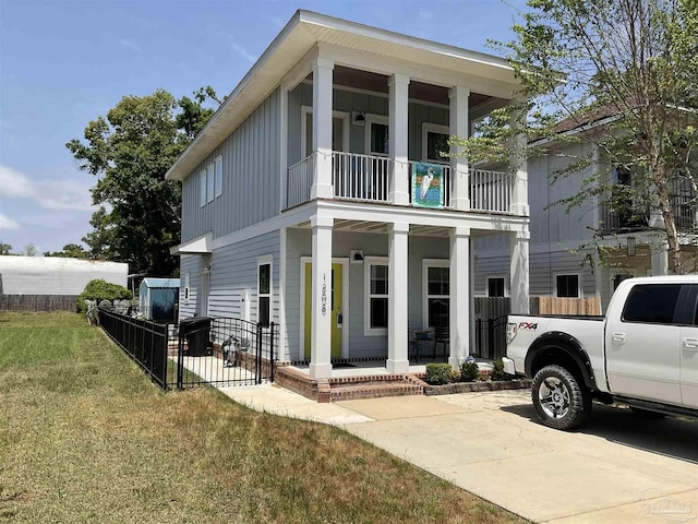 greek revival inspired property featuring fence, board and batten siding, a front yard, a balcony, and covered porch