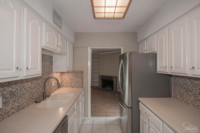 kitchen with light wood-type flooring, white cabinets, backsplash, a fireplace, and sink