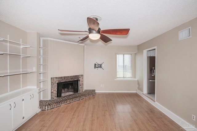 unfurnished living room featuring light hardwood / wood-style floors, a brick fireplace, ceiling fan, and a textured ceiling