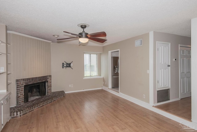 unfurnished living room with light hardwood / wood-style floors, a brick fireplace, ceiling fan, and a textured ceiling