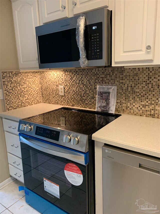 kitchen with appliances with stainless steel finishes, light tile patterned flooring, decorative backsplash, and white cabinets