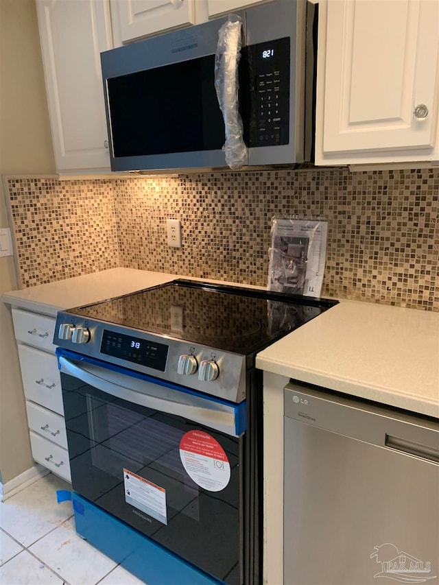 kitchen with light tile patterned floors, decorative backsplash, white cabinets, and stainless steel appliances