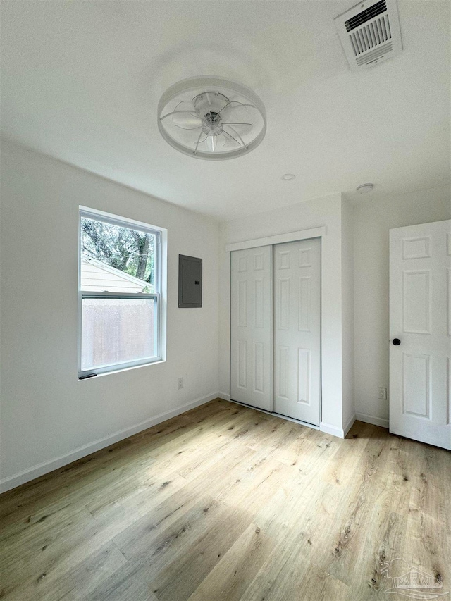 unfurnished bedroom featuring electric panel, light hardwood / wood-style flooring, and a closet