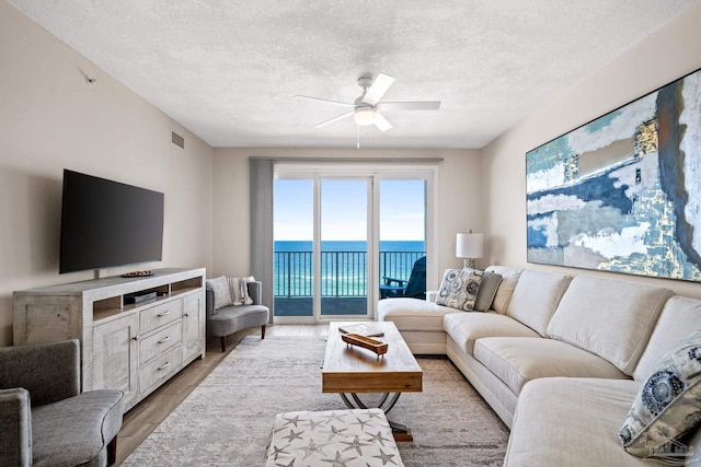 living room featuring light wood-type flooring, ceiling fan, and a textured ceiling