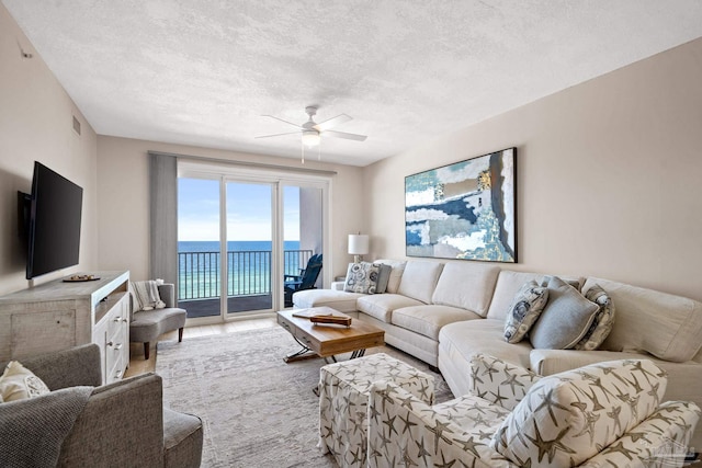 living room with a water view, ceiling fan, a textured ceiling, and light hardwood / wood-style flooring