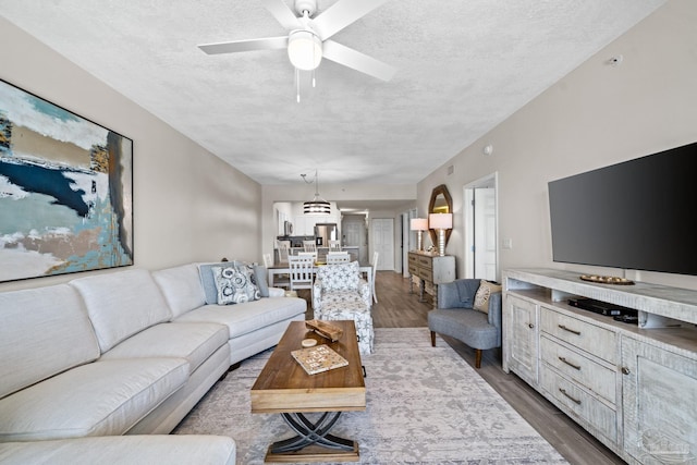 living room featuring wood-type flooring, ceiling fan with notable chandelier, and a textured ceiling