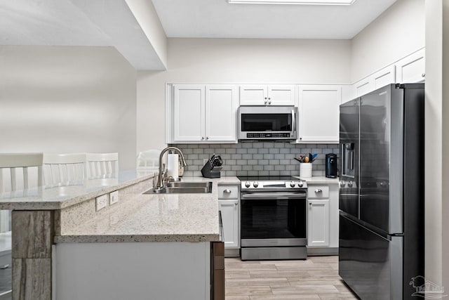 kitchen with kitchen peninsula, sink, white cabinetry, light stone countertops, and stainless steel appliances