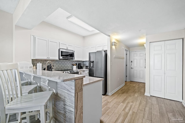 kitchen with kitchen peninsula, appliances with stainless steel finishes, decorative backsplash, a kitchen breakfast bar, and white cabinets