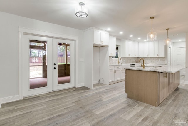 kitchen featuring white cabinetry, light stone counters, french doors, a kitchen island with sink, and pendant lighting