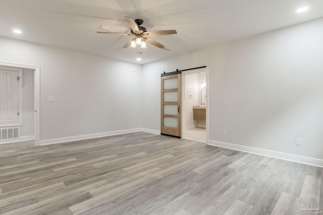 empty room with ceiling fan, light hardwood / wood-style flooring, and a barn door