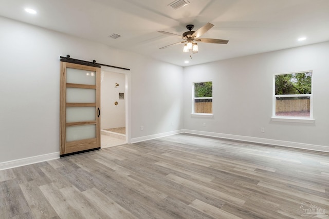 unfurnished room with light wood-type flooring, ceiling fan, and a barn door