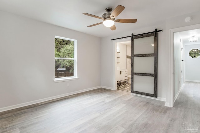 unfurnished bedroom with ceiling fan, light hardwood / wood-style floors, and a barn door