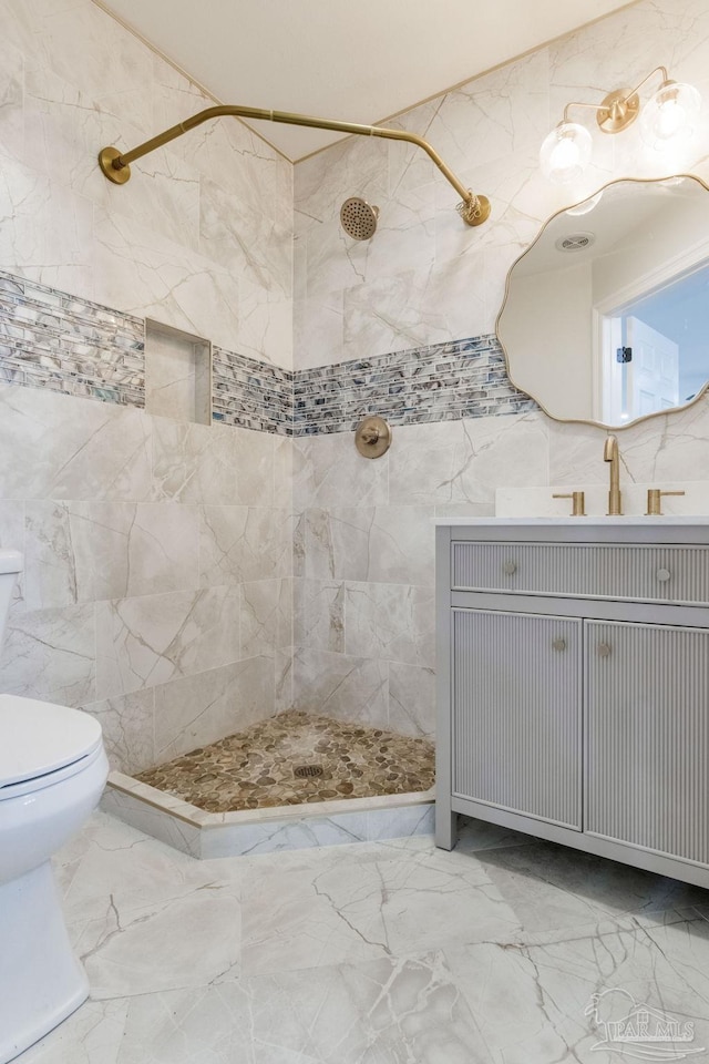 bathroom with a tile shower, vanity, and toilet