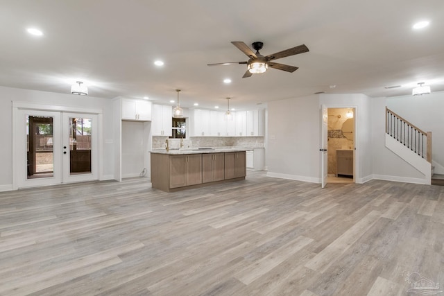 kitchen featuring a large island, hanging light fixtures, light wood-type flooring, white cabinets, and backsplash