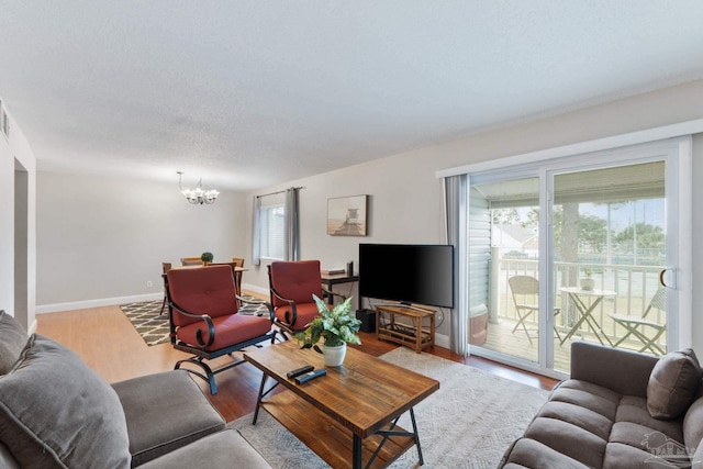 living room with an inviting chandelier, a textured ceiling, baseboards, and wood finished floors